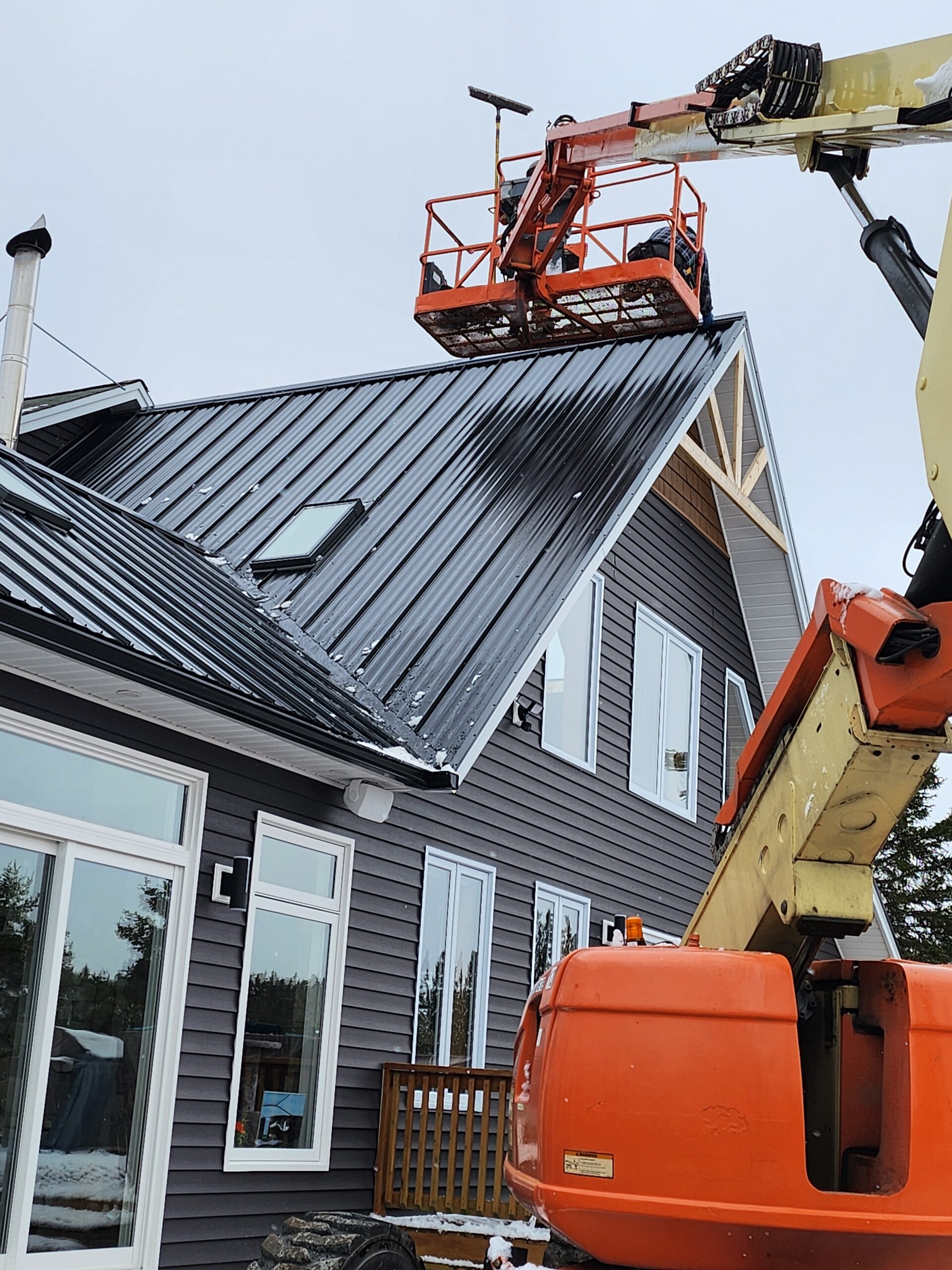 Freedom Metal Roofing crew using a JLG lift to finish a steel roof on a two-story house in NL
