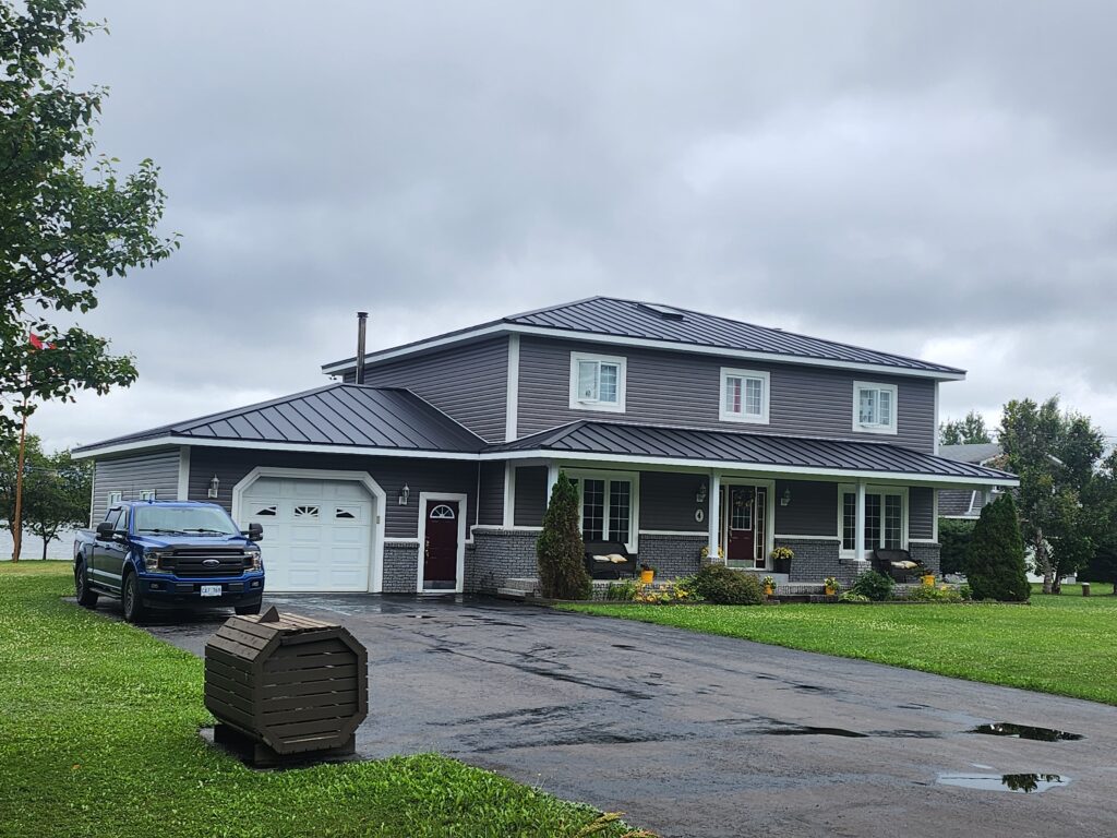 Black steel hip roof on main house with partial hip garage and front overhang installed by Freedom Metal Roofing NL
